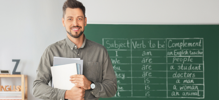 Ein freundlicher Lehrer steht vor einer Schultafel