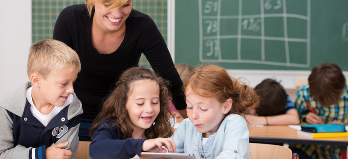 Eine Lehrerin mit Kindern samt Tablet-PC im Unterricht